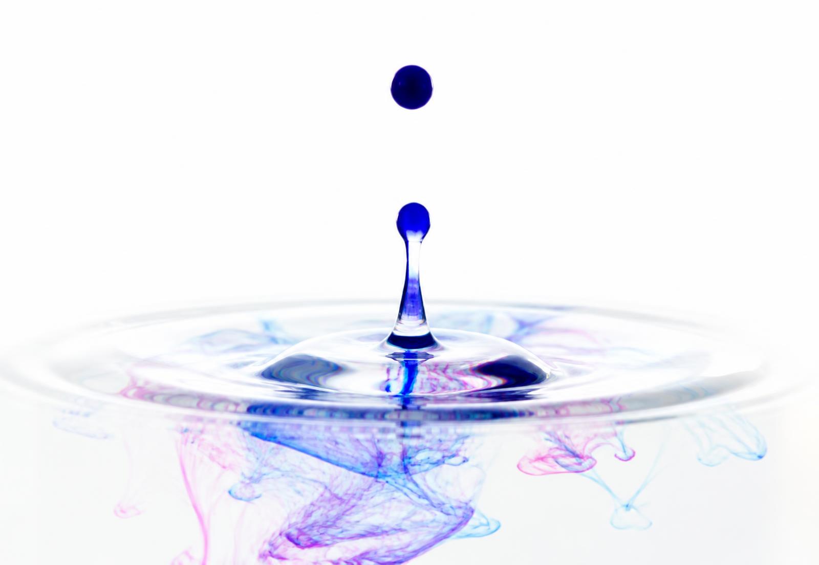Blauer Tintentropfen in Wasser mit feinen Cyan- und Magenta-Schlieren